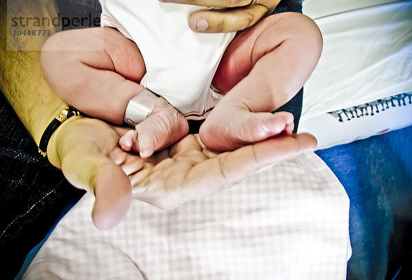 Füße eines Neugeborenen an der Hand eines Mannes