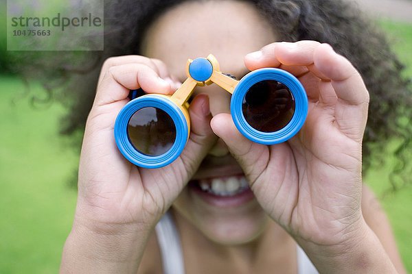 MODELL FREIGEGEBEN. Mädchen benutzt ein Fernglas in einem Park. Ferngläser enthalten Vergrößerungslinsen  die zum Betrachten entfernter Objekte verwendet werden.