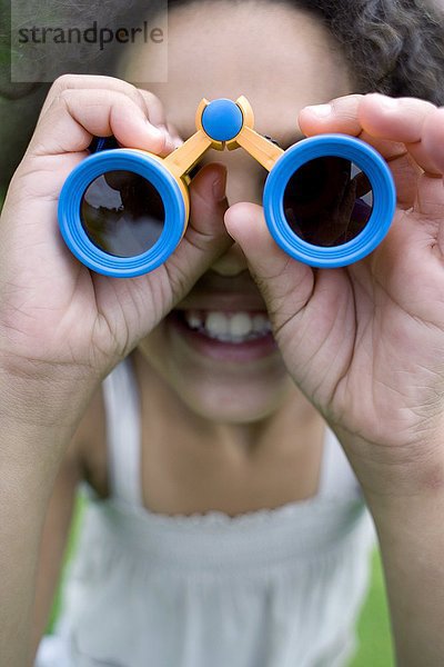 MODELL FREIGEGEBEN. Mädchen benutzt ein Fernglas in einem Park. Ferngläser enthalten Vergrößerungslinsen  die zum Betrachten entfernter Objekte verwendet werden.