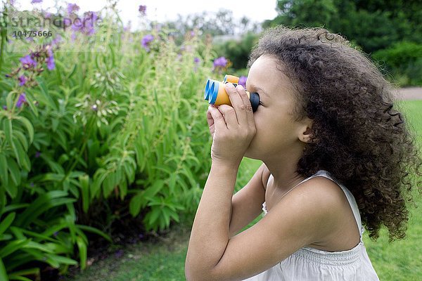 MODELL FREIGEGEBEN. Mädchen benutzt ein Fernglas in einem Park. Ferngläser enthalten Vergrößerungslinsen  die zum Betrachten entfernter Objekte verwendet werden.