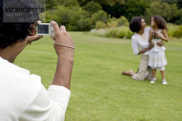 MODELL FREIGEGEBEN. Verwendung einer Digitalkamera. Vater  der seine Partnerin und seine Tochter fotografiert Verwendung einer Digitalkamera