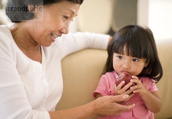 MODELL FREIGEGEBEN. Großmutter und Enkelin. Die Großmutter ermutigt ihre Enkelin  einen Apfel zu essen  ein gesundes Lebensmittel und eine Quelle von Vitaminen und Ballaststoffen Großmutter und Enkelin