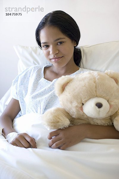 MODELL FREIGEGEBEN. Teenager-Krankenhaus-Patient. Teenager-Mädchen kuschelt einen Teddybär in einem Krankenhausbett Teenager-Krankenhaus-Patient