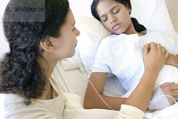 MODELL FREIGEGEBEN. Besuch im Krankenhaus. Mutter hält die Hand ihrer Tochter  während sie in einem Krankenhausbett schläft Krankenhausbesuch