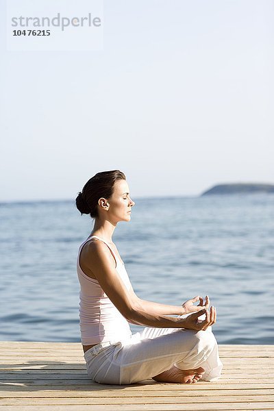 MODELL FREIGEGEBEN. Frau führt eine Yoga-Übung am Meer durch Frau führt Yoga-Übung durch