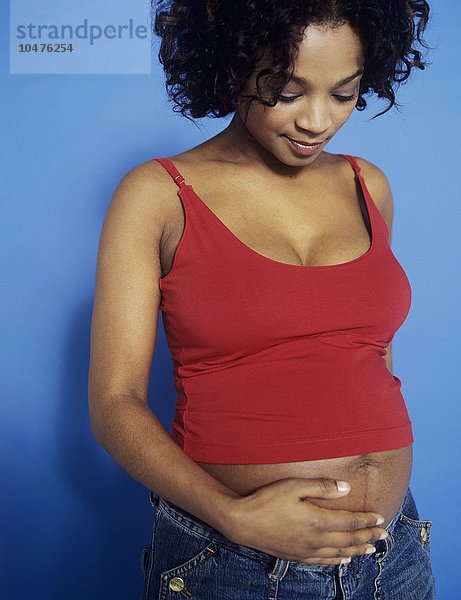 MODELL FREIGEGEBEN. Eine schwangere Frau hält ihren geschwollenen Bauch. Sie ist in der 30. Woche schwanger. Eine Schwangerschaft dauert zwischen 37 und 42 Wochen. Schwangere Frau