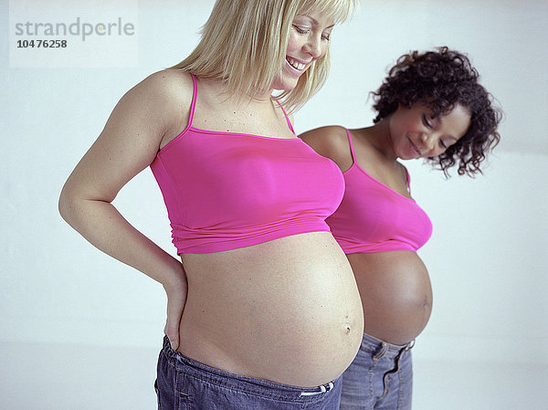 MODELL FREIGEGEBEN. Schwangere Frauen  die ihre geschwollenen Bäuche miteinander vergleichen. Sie sind beide im 7. Monat schwanger. Eine Vollschwangerschaft dauert etwa 9 Monate (zwischen 37 und 42 Wochen). Schwangere Frauen