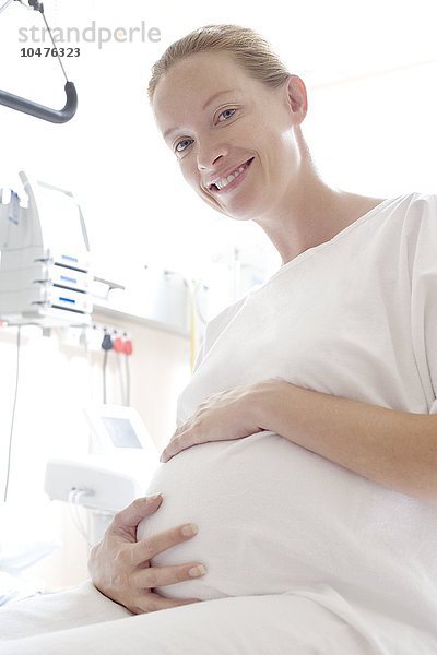 MODELL FREIGEGEBEN. Schwangere Frau auf einer Entbindungsstation  die ihren geschwollenen Bauch festhält Schwangere Frau