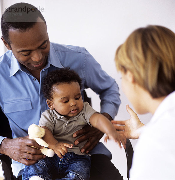 MODELL FREIGEGEBEN. Pädiatrische Untersuchung. Arzt untersucht einen 5 Monate alten Jungen  der auf dem Schoß seines Vaters sitzt Pädiatrische Untersuchung