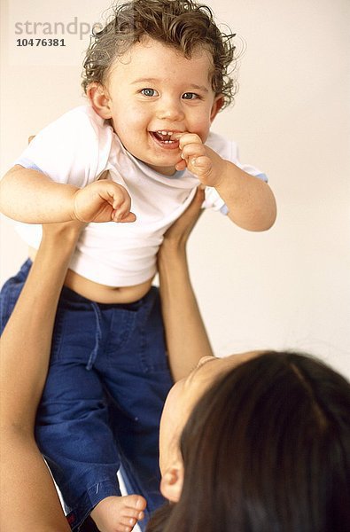 MODELL FREIGEGEBEN. Kleiner Junge und Mutter. 9 Monate altes Baby lächelt  als seine Mutter ihn über ihren Kopf hebt Baby und Mutter