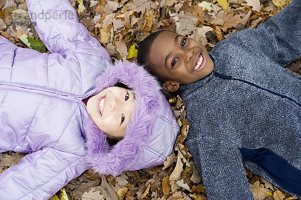 MODELL FREIGEGEBEN. Lächelndes Mädchen und Junge auf Herbstblättern liegend Lächelnde Kinder auf Herbstblättern liegend