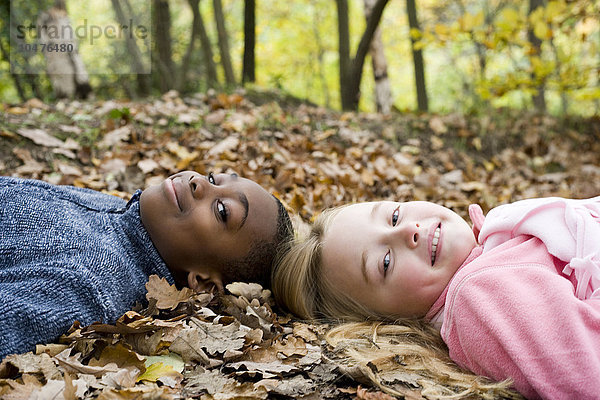 MODELL FREIGEGEBEN. Lächelnde Jungen und Mädchen auf Herbstblättern liegend Lächelnde Kinder auf Herbstblättern liegend