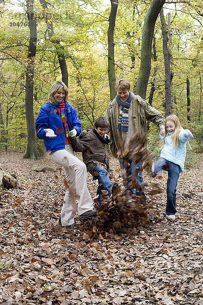 MODELL FREIGEGEBEN. Kicken Herbstblätter. Mutter und Vater und Sohn und Tochter treten Blätter in einem Wald im Herbst Familie spielt in einem Wald