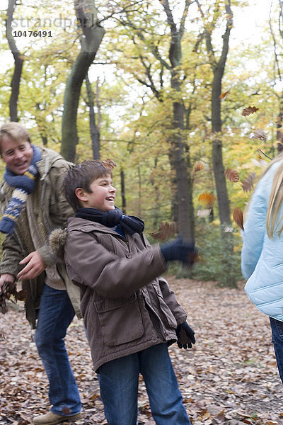MODELL FREIGEGEBEN. Spielen mit Herbstblättern. Vater und Sohn und Tochter spielen mit Blättern in einem Wald im Herbst Vater und Kinder spielen in einem Wald