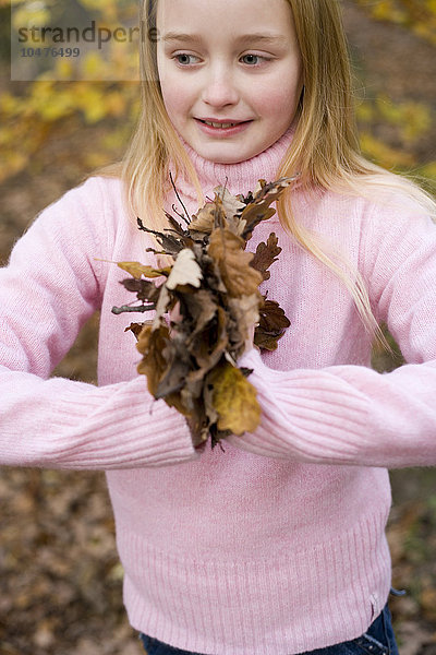 MODELL FREIGEGEBEN. Mädchen hält Herbstblätter und bereitet sich darauf vor  sie zu werfen  während sie im Wald spielt Mädchen hält Herbstblätter