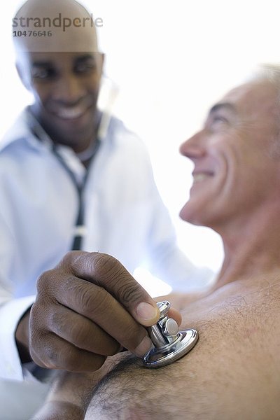 MODELL FREIGEGEBEN. Medizinische Konsultation. Ein Arzt hört mit einem Stethoskop die Brust eines Patienten ab. Ein Stethoskop ist ein medizinisches Gerät  mit dem man Geräusche im Körper abhören kann. Medizinische Beratung