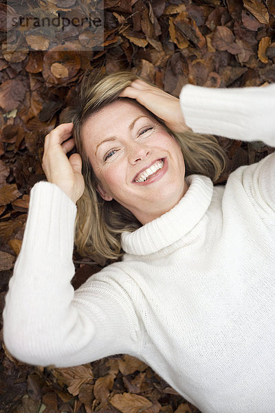 MODELL FREIGEGEBEN. Lächelnde Frau auf Herbstblättern liegend Lächelnde Frau auf Herbstblättern liegend