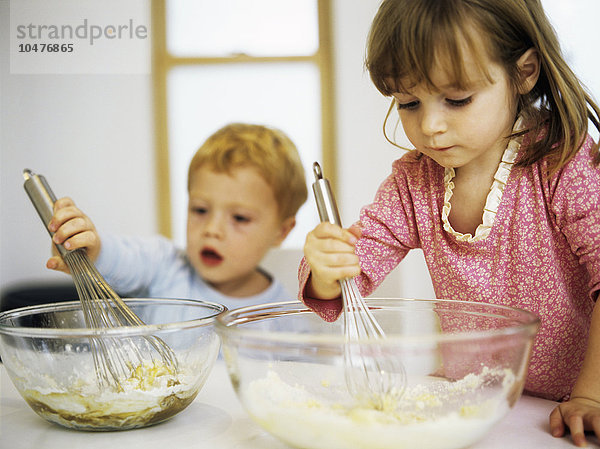 MODELL FREIGEGEBEN. Kuchen backen. Zwei dreijährige Kinder mischen Eier  Zucker und Mehl in einer Rührschüssel Kuchen backen