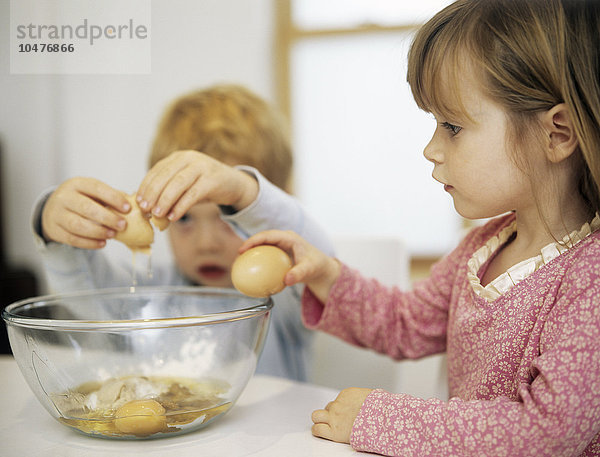 MODELL FREIGEGEBEN. Kuchen backen. Zwei dreijährige Kinder schlagen Eier an der Seite einer Rührschüssel auf und fügen sie einer Kuchenmischung hinzu Kuchen backen
