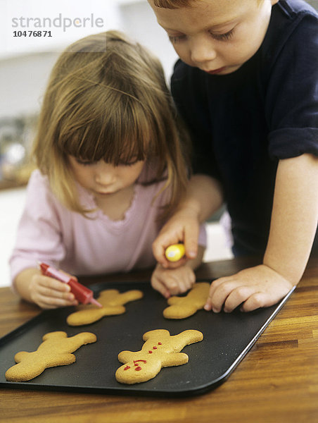 MODELL FREIGEGEBEN. Kekse backen. Zwei dreijährige Kinder verzieren frisch gebackene Kekse mit farbigem Zuckerguss Kekse backen