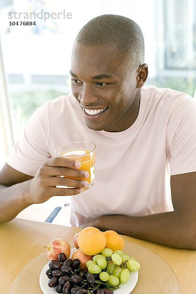 MODELL FREIGEGEBEN. Mann trinkt Orangensaft an einem Esstisch Mann trinkt Orangensaft