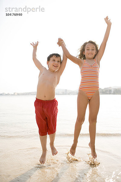 MODELL FREIGEGEBEN. Glückliche Kinder  die an einem Strand über die Wellen springen Glückliche Kinder