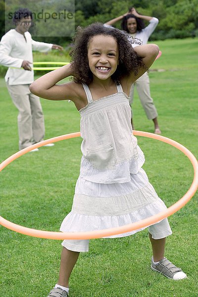 MODELL FREIGEGEBEN. Mädchen spielt mit einem Hula-Hoop-Reifen mit ihrer Familie in einem Garten Mädchen spielt mit einem Hula-Hoop-Reifen