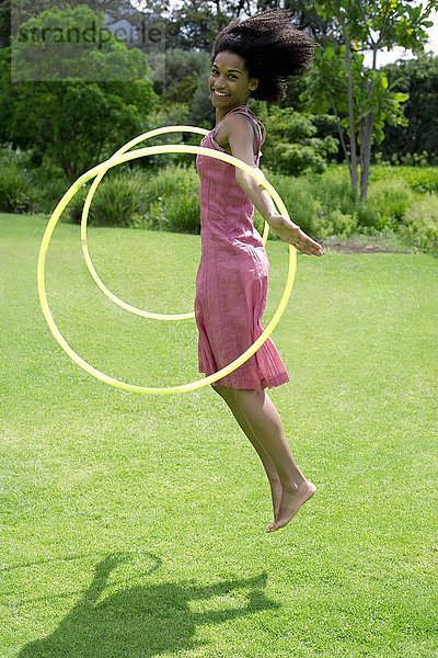 MODELL FREIGEGEBEN. Frau spielt mit Hula-Hoop-Reifen in einem Garten Frau spielt mit Hula-Hoop-Reifen