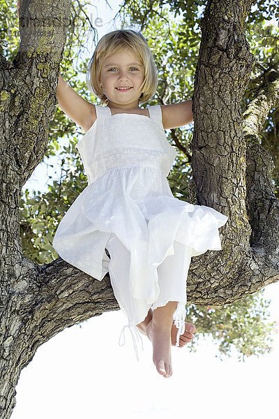 MODELL FREIGEGEBEN. Mädchen sitzt auf einem Baum  auf den sie geklettert ist Mädchen sitzt auf einem Baum