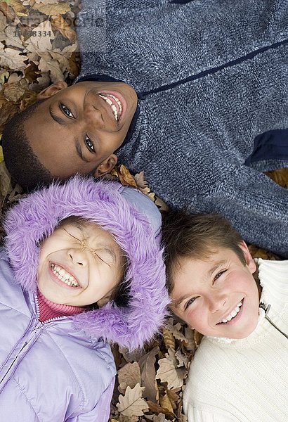 Lächelnde Kinder auf Herbstblättern liegend