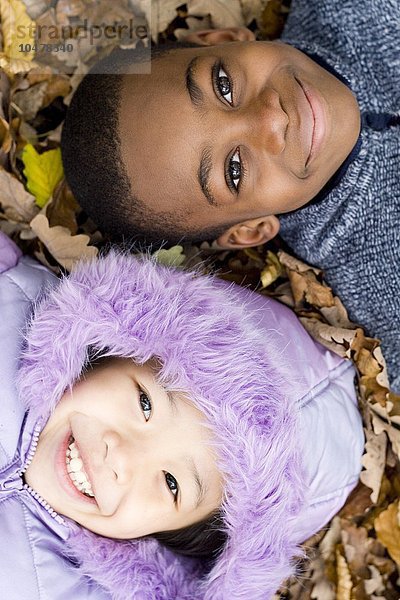 Lächelnde Kinder auf Herbstblättern liegend