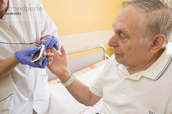 Reportage in der Abteilung für Innere Medizin und Geriatrie im Krankenhaus Saint-Philibert in Lille  Frankreich. Eine Krankenschwester überprüft den Blutzuckerspiegel eines Patienten mit einem Glukosemessgerät in seinem Krankenzimmer.