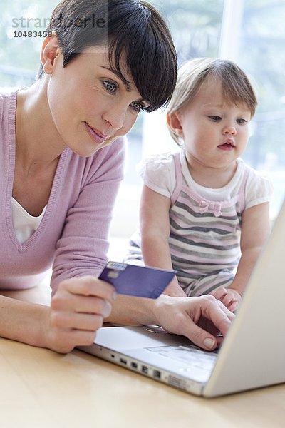 MODELL FREIGEGEBEN. Online-Einkauf. Mutter kauft online ein  während ihre 15 Monate alte Tochter zuschaut Online-Shopping