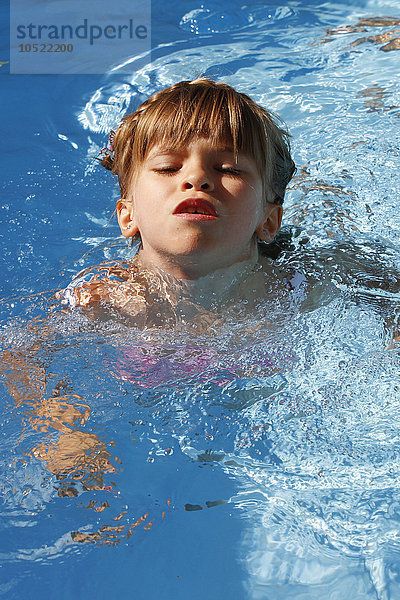 Ein 6-jähriges Mädchen schwimmt zum ersten Mal ohne Armbinden in einem Schwimmbad.