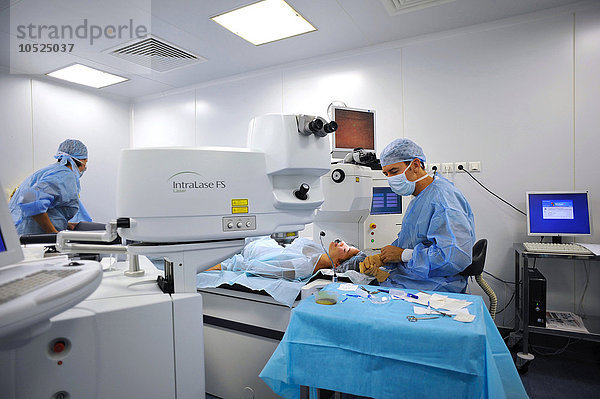 Reportage über refraktive Augenchirurgie in der Stiftung für Augenheilkunde Adolphe de Rothschild in Paris  Frankreich. Augenoperation mit einem Femtosekundenlaser und einem Excimerlaser. Der Femtosekundenlaser schneidet die Hornhaut ein  um einen Hornhautdeckel (violett) zu erzeugen  dann hebt der Chirurg den Flap an  um das Auge mit dem Excimer-Laser zu behandeln. Die Hornhautlamelle wird dann ohne Nähte wieder an ihren Platz gesetzt. Diese Technik wird zur Behandlung von Kurzsichtigkeit  Alterssichtigkeit  Astigmatismus und Weitsichtigkeit eingesetzt. Operationssaal mit dem Excimer-Laser auf der rechten Seite und dem Femtosekundenlaser auf der linken Seite.