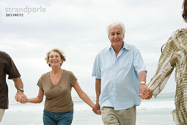 Vier ältere Erwachsene halten sich am Strand an den Händen.