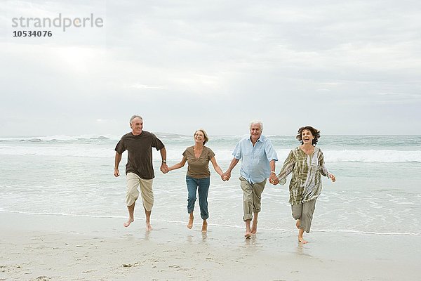 Vier ältere Erwachsene laufen am Strand entlang