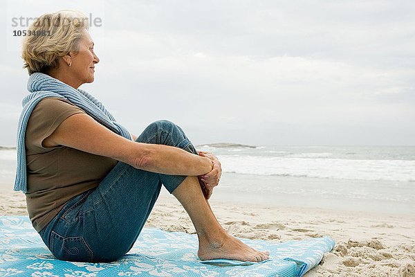 Ältere erwachsene Frau saß am Strand.