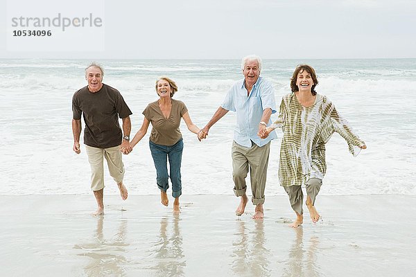 Vier ältere Erwachsene  die an einem Strand entlang laufen.