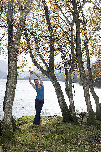 Frau praktiziert Yogastellung unter Bäumen