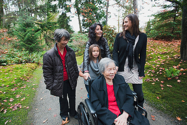 Mehrgenerationen-Familie schiebt ältere Frau im Rollstuhl