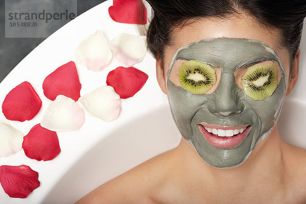 Frau mit Gesichtsmaske und Kiwi im Bad