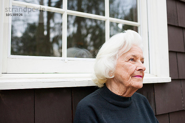 Porträt einer älteren Frau vor dem Haus mit Blick nach draußen