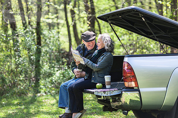 Seniorenpaar beim Lesen der Karte auf dem Kofferraum im Wald