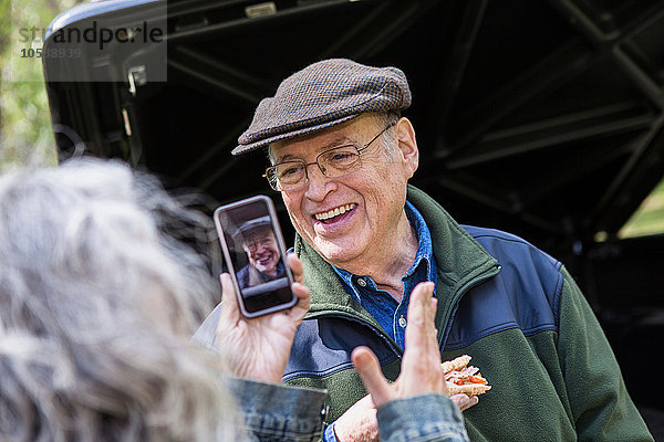 Seniorin beim Fotografieren von lächelndem Mann im Freien
