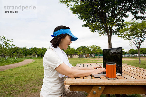 Frau mit Laptop auf der Picknickbank im Park