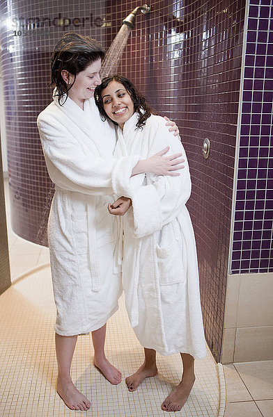 Frauen in Bademänteln umarmend in der Dusche