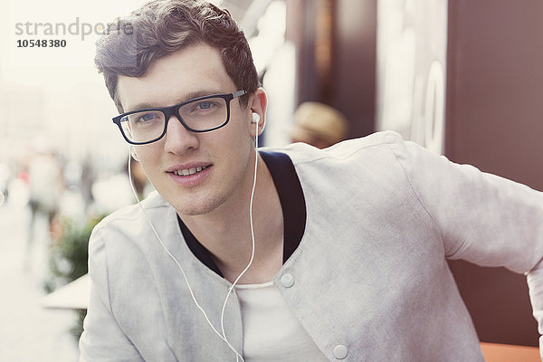 Porträt eines lächelnden Mannes mit Brille  der Musik über Kopfhörer hört.