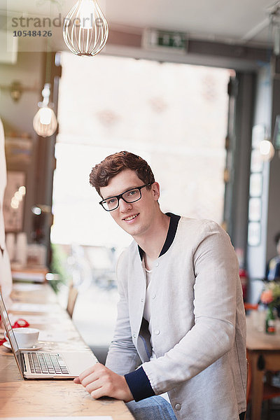 Portrait lächelnder Mann mit Brille mit Laptop im Cafe