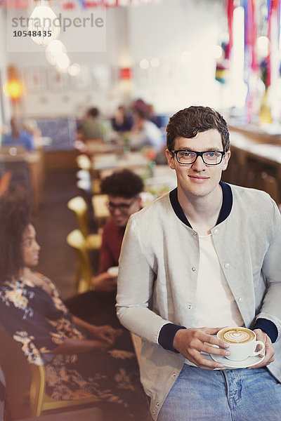 Portrait lächelnder Mann mit Brille trinkt Cappuccino im Cafe